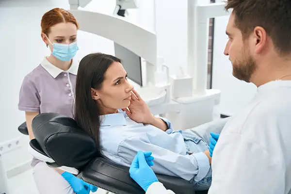 A dentist and assistant examining a female patient in a clinic, assessing symptoms of tooth sensitivity.